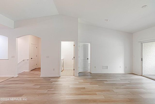 interior space with ensuite bathroom, washer / dryer, light hardwood / wood-style flooring, and high vaulted ceiling