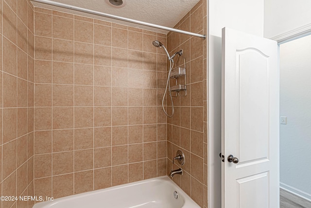 bathroom with a textured ceiling and tiled shower / bath combo