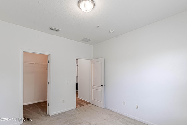 unfurnished bedroom featuring a walk in closet, light carpet, and a closet