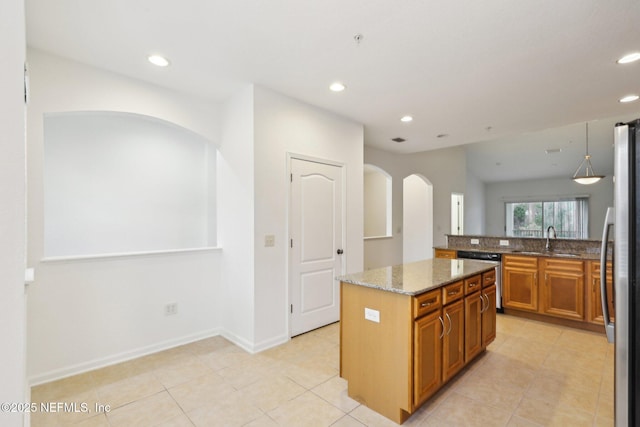 kitchen with appliances with stainless steel finishes, a kitchen island, sink, light tile patterned flooring, and light stone counters