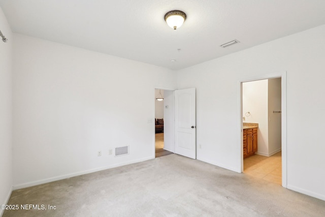 unfurnished bedroom featuring light colored carpet and ensuite bathroom