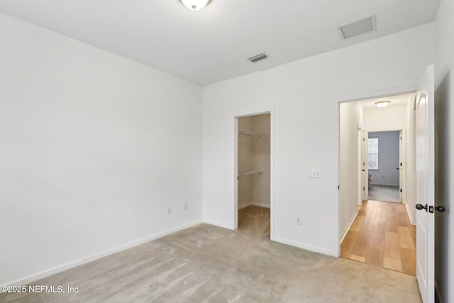 unfurnished bedroom with light carpet, a closet, and a walk in closet