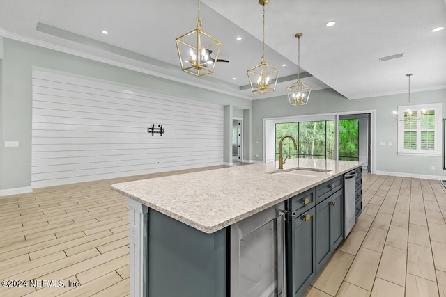 kitchen featuring sink, hanging light fixtures, ornamental molding, an island with sink, and a tray ceiling