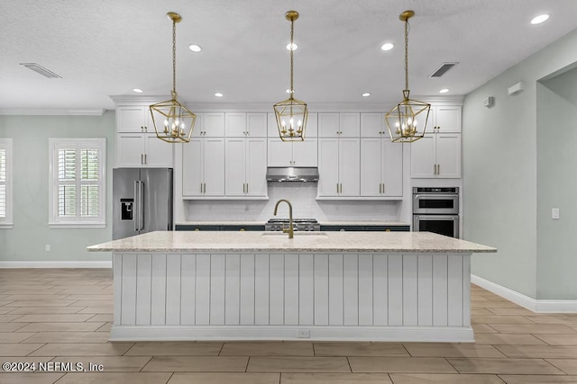 kitchen featuring light stone countertops, pendant lighting, stainless steel appliances, and an island with sink