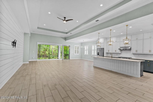 unfurnished living room with a raised ceiling, ceiling fan, light hardwood / wood-style flooring, and sink