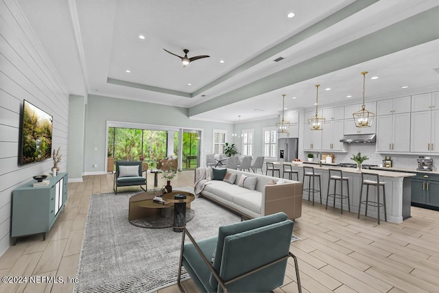 living room with a tray ceiling, light hardwood / wood-style floors, and ceiling fan with notable chandelier