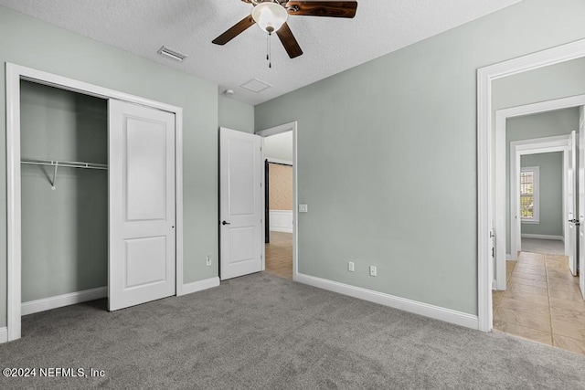 unfurnished bedroom featuring light carpet, a textured ceiling, a closet, and ceiling fan