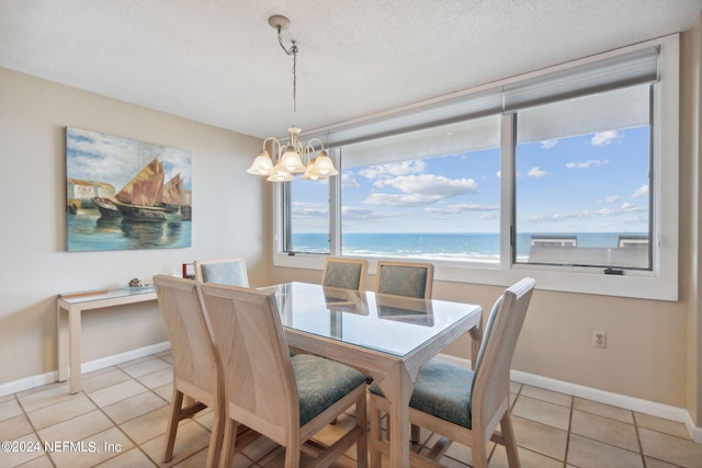 tiled dining room with a textured ceiling, a water view, a beach view, and an inviting chandelier