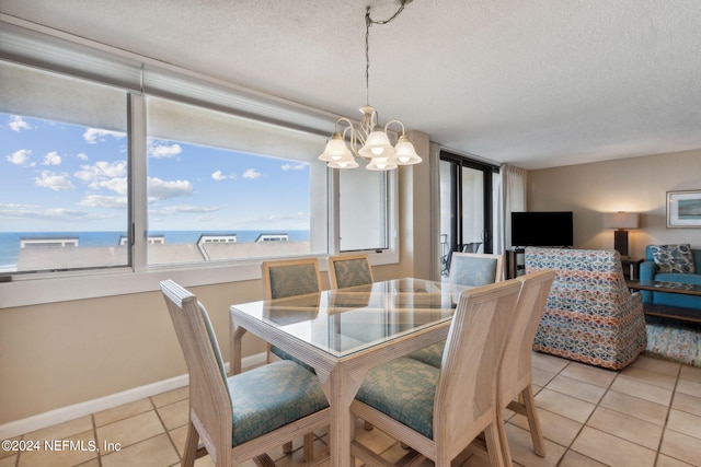 tiled dining space with a water view, a textured ceiling, and an inviting chandelier