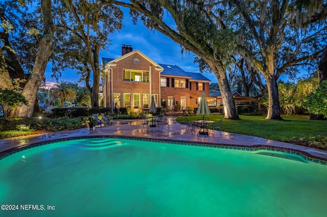 pool at dusk featuring a lawn and a patio area