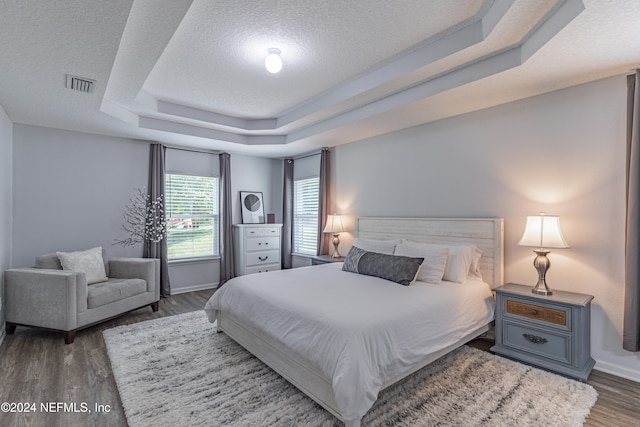 bedroom featuring a textured ceiling, dark hardwood / wood-style flooring, and a tray ceiling