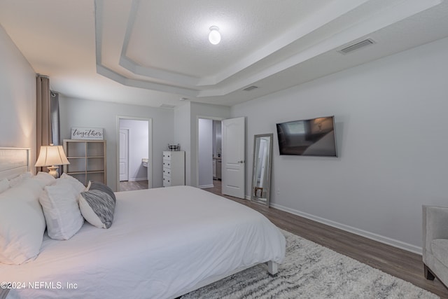 bedroom with dark hardwood / wood-style floors, ensuite bathroom, and a tray ceiling