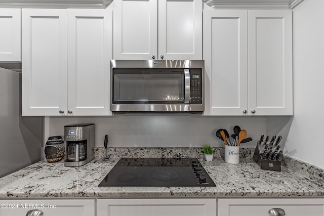 kitchen featuring white cabinets, black electric stovetop, and light stone countertops