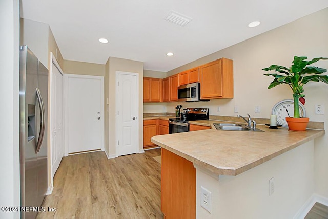 kitchen featuring appliances with stainless steel finishes, sink, light wood-type flooring, and kitchen peninsula