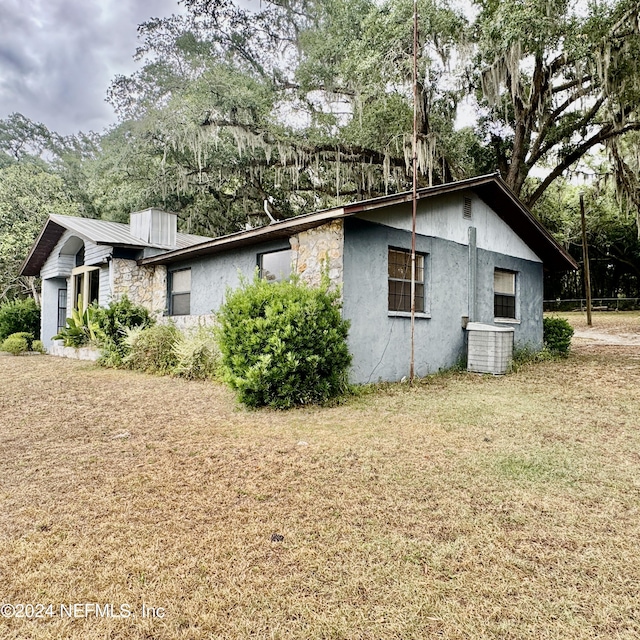 view of side of property featuring central AC, a lawn, and stucco siding