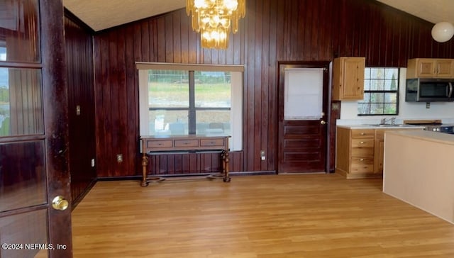 kitchen with wooden walls, lofted ceiling, stainless steel microwave, light countertops, and light wood-type flooring