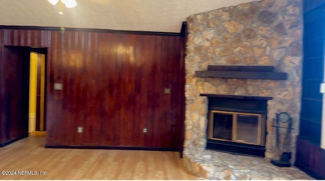 unfurnished living room with a stone fireplace, a textured ceiling, and wood-type flooring