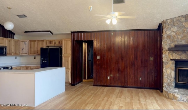 kitchen featuring light wood-style floors, a fireplace, light countertops, and black fridge