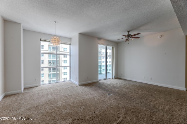 carpeted empty room with ceiling fan with notable chandelier, a textured ceiling, and a healthy amount of sunlight