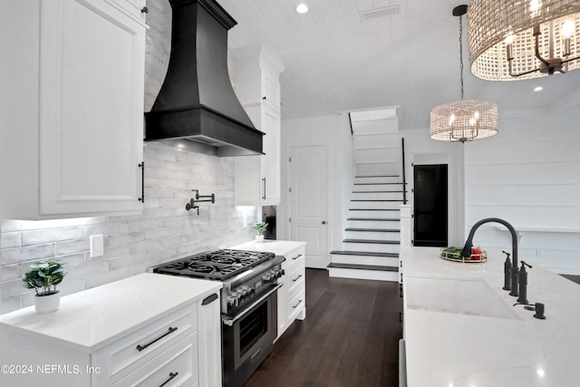 kitchen with high end stainless steel range, white cabinets, premium range hood, and decorative light fixtures