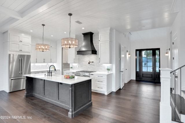 kitchen with an island with sink, appliances with stainless steel finishes, dark wood-type flooring, and custom range hood