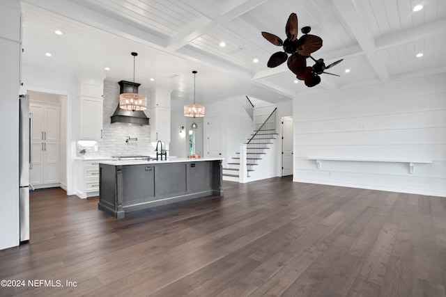 kitchen featuring a large island with sink, dark wood-type flooring, ceiling fan with notable chandelier, pendant lighting, and custom exhaust hood