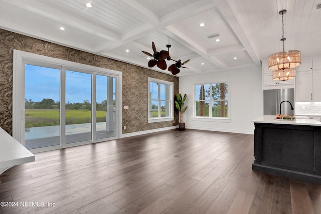 unfurnished living room featuring beamed ceiling, dark hardwood / wood-style floors, sink, ceiling fan with notable chandelier, and coffered ceiling