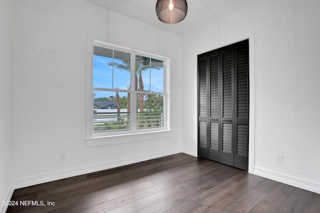 unfurnished bedroom featuring a closet, multiple windows, and dark hardwood / wood-style flooring