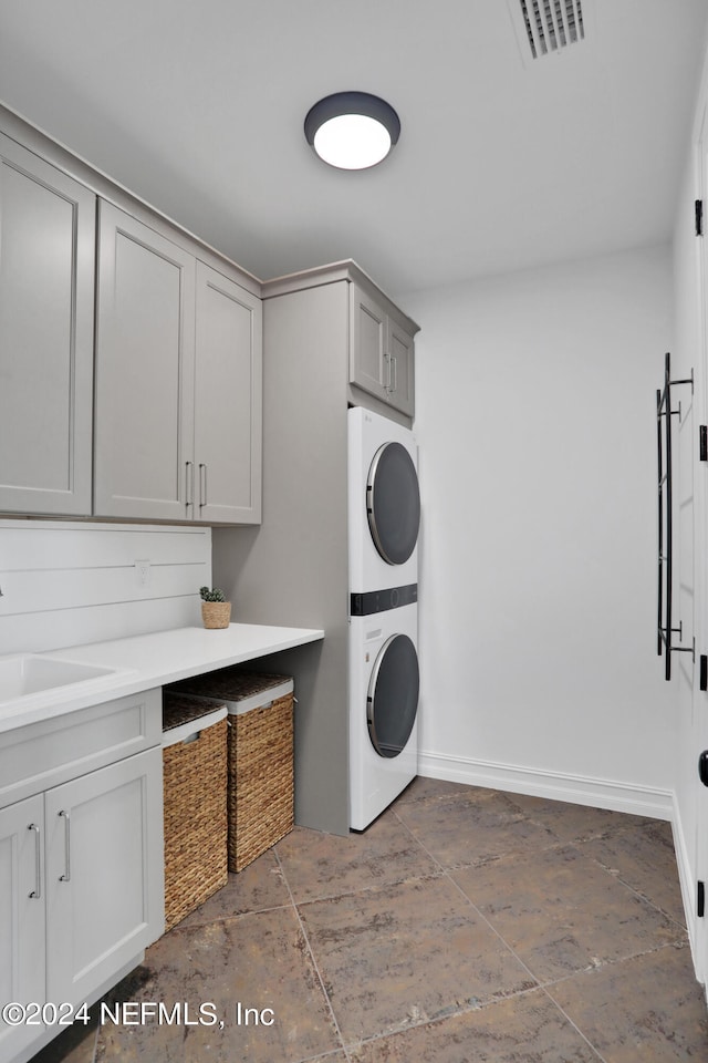 laundry room featuring stacked washer and dryer, sink, and cabinets