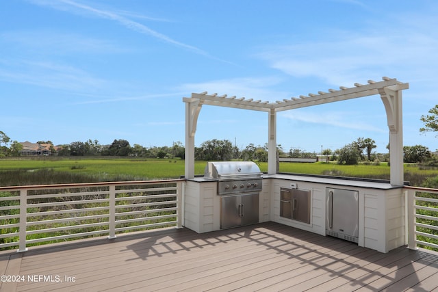 wooden terrace with area for grilling, a pergola, and exterior kitchen