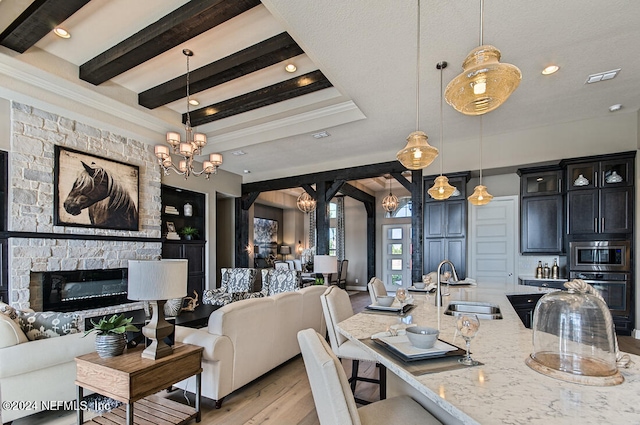 dining area with sink, an inviting chandelier, light wood-type flooring, built in features, and a stone fireplace