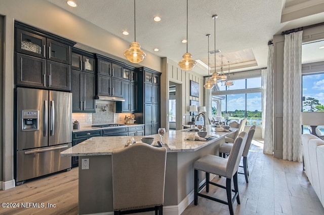 kitchen with pendant lighting, a center island with sink, a breakfast bar, a tray ceiling, and appliances with stainless steel finishes