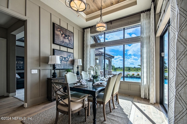 dining space with a raised ceiling, wood-type flooring, a water view, and ornamental molding