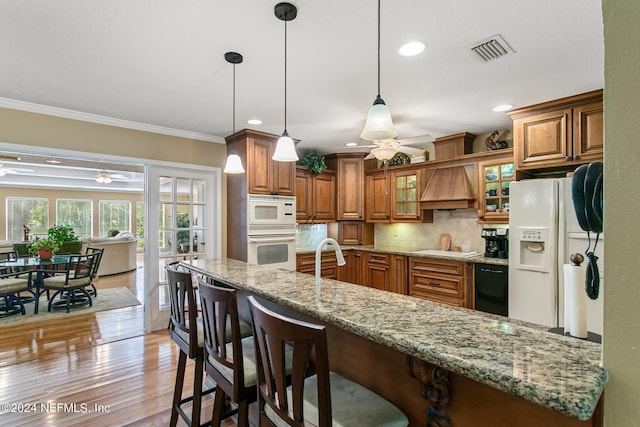 kitchen featuring white appliances, visible vents, brown cabinetry, a ceiling fan, and premium range hood