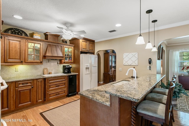 kitchen with white appliances, arched walkways, brown cabinetry, premium range hood, and a sink