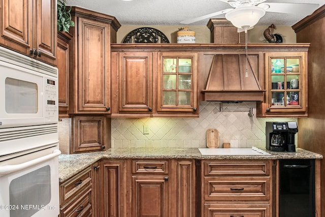 kitchen with tasteful backsplash, white appliances, glass insert cabinets, and custom range hood