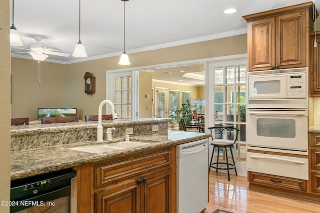 kitchen with a warming drawer, ornamental molding, brown cabinetry, a sink, and white appliances