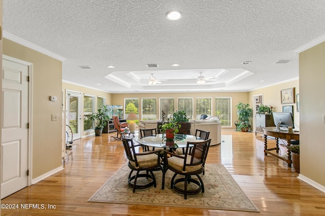 dining space featuring a tray ceiling, ornamental molding, light wood-type flooring, and visible vents