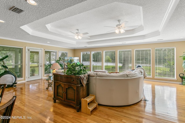 living area featuring light wood-style flooring, visible vents, a raised ceiling, and ornamental molding