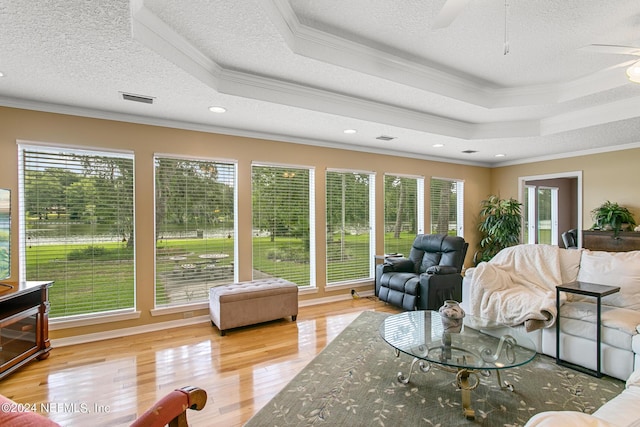 living area with a wealth of natural light, crown molding, a tray ceiling, and wood finished floors