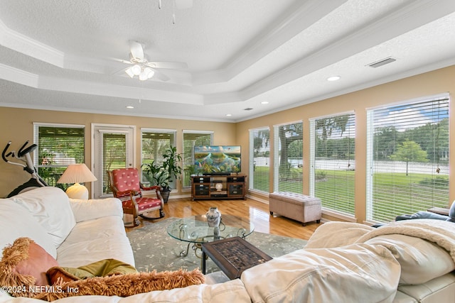 living area featuring a ceiling fan, a tray ceiling, crown molding, and wood finished floors