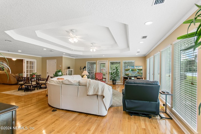 living area featuring a textured ceiling, a tray ceiling, visible vents, and light wood-style floors