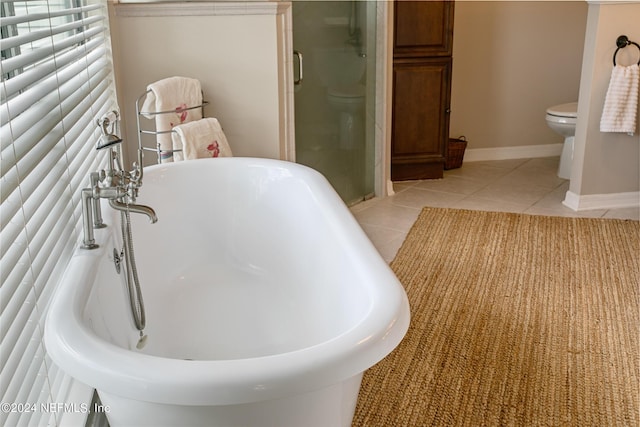 bathroom with toilet, a stall shower, tile patterned flooring, a freestanding tub, and baseboards