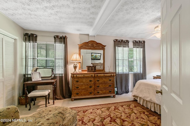 bedroom with a textured ceiling, ceiling fan, a closet, beam ceiling, and carpet