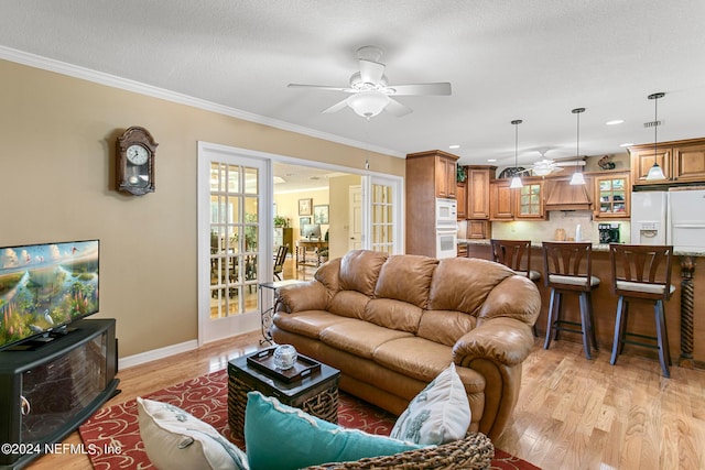 living area featuring light wood-type flooring, baseboards, a ceiling fan, and crown molding