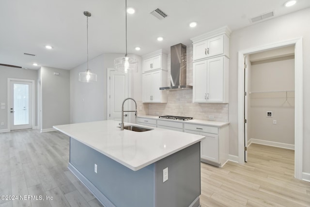 kitchen with a kitchen island with sink, stainless steel gas cooktop, sink, wall chimney range hood, and white cabinets