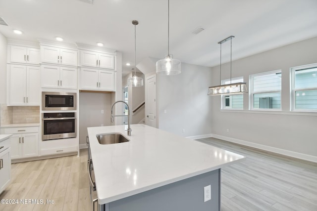 kitchen with a kitchen island with sink, white cabinets, oven, sink, and hanging light fixtures