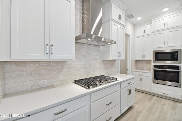 kitchen featuring white cabinetry, wall chimney exhaust hood, stainless steel appliances, tasteful backsplash, and light hardwood / wood-style flooring