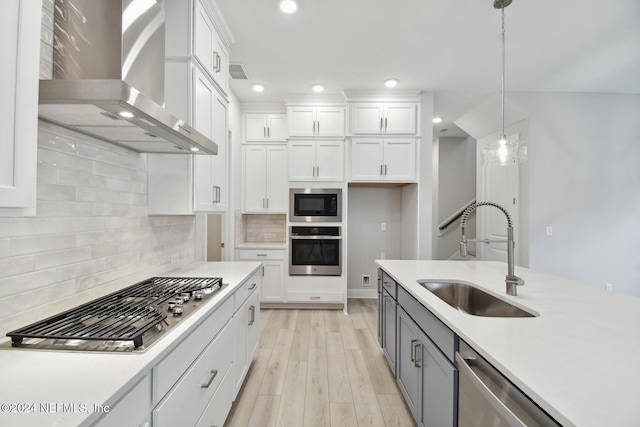 kitchen featuring wall chimney range hood, sink, hanging light fixtures, white cabinetry, and stainless steel appliances