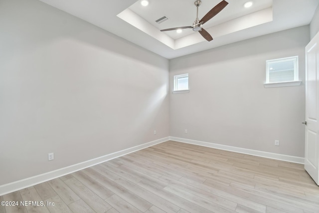 empty room with a tray ceiling, ceiling fan, and light hardwood / wood-style floors